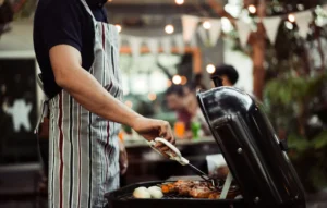 Henkilö grillaamassa ruokaa hiiligrillillä ulkona.