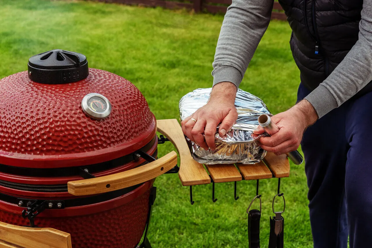 Punainen kamado-grilli käytössä pihalla ruoan valmistuksen yhteydessä.