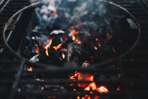Hiiligrillin hehkuvat hiilet ja savua nousemassa, symboloiden erilaisten hiiligrillien toimintaa ja eroja.