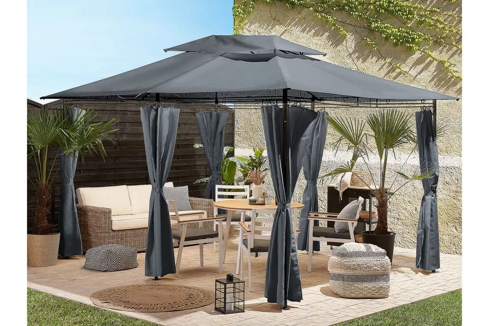 Tilava harmaa paviljonki verhoilla, sijoitettu suojaisalle patiolle, alla ruokailuryhmä ja sohvakalusteet, mökkimäinen tunnelma