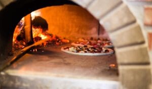 Puulämmitteinen pizzauuni, jossa pizza kypsyy avotulen lämmössä. Perinteinen pizzauuni tuo aitoa italialaista makua kotiin.