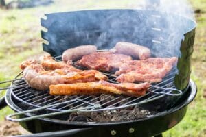 Hiiligrilli täynnä grillattavaa ruokaa, kuten pihvejä, pekonia ja makkaroita, savun noustessa ilmaan.