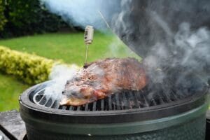 Grillissä kypsyvä savustettu liha lämpömittarilla kamado-tyyppisessä hiiligrillissä ulkona puutarhassa.