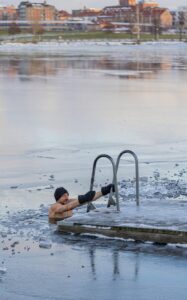 Mies avantouimassa jäisessä vedessä, pitäen kiinni tikkaista ja nauttien kylmävesiterapian hyödyistä.