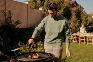 Mies grillaamassa kanaa hiiligrillissä puutarhassa – täydellinen esimerkki rennosta ja edullisesta kesägrillauksesta kotipihalla.