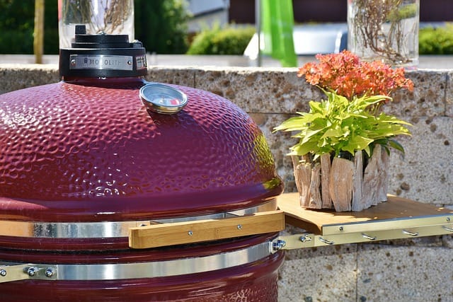 Punainen kamadogrilli terassilla, vieressä koristekasveja – vertailussa Kamado Sumo ja Big Green Egg vuoden 2025 näkökulmasta.