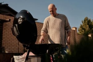 Mies grillaamassa pallohiiligrillillä kotipihalla aurinkoisena päivänä – grillaus käynnissä kannellinen grilli auki.