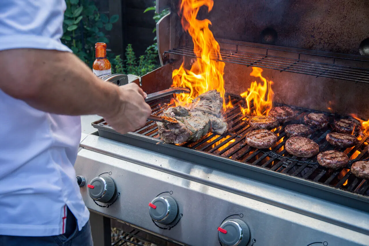 Weber kaasugrilli käytössä, liekkejä ja grillattavaa ruokaa ritilällä.