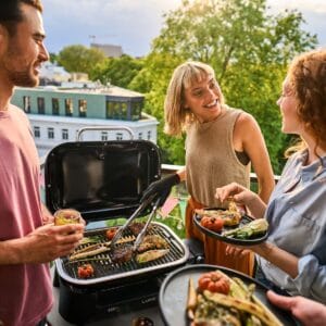 Kolme ihmistä grillaamassa Weber Lumin Compact -sähkögrillillä parvekkeella – mukana vuoden 2025 Top 3 sähkögrillivertailussa.