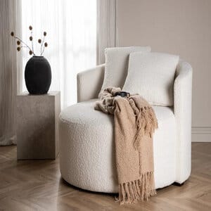 Kelso 2:n istuttava pyöreä muotoiltu valkoinen sohva, päällä beige viltti ja kaksi tyynyä, taustalla kivipöytä ja vaalea verho.