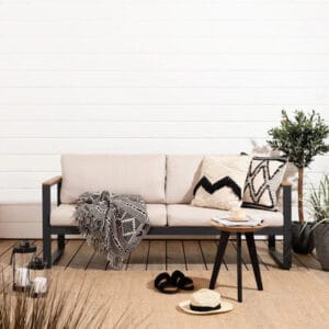 Vaalea Aava 3-istuttava terassisohva mustilla kehyksillä, koristetyynyillä ja viltillä varustettuna terassilla