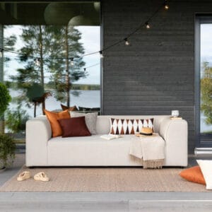 Vaalea beige Huuma 3-istuttava terassisohva terassilla, koristetyynyillä ja lämpimillä sävyillä sisustettuna