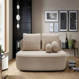 Hiekanvärinen Mooda Calvin 3-istuttava vuodesohva tyylikkäässä olohuoneessa, koristeellisilla soikeilla tyynyillä