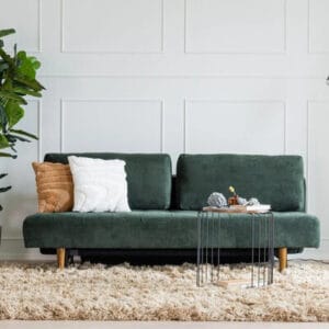 Tummanvihreä Naava 3-istuttava vuodesohva vaalealla seinällä, koristetyynyillä ja modernilla metallipöydällä