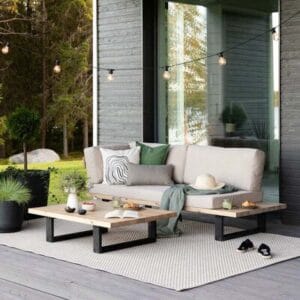 Saima divaani terassilla, mustarunkoinen ja beigeillä pehmusteilla, ympärillään vehreä piha ja tunnelmavalot