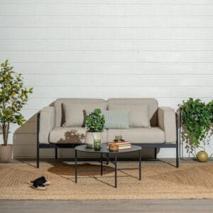 Vaaleanbeige Trondheim 2,5-istuttava terassisohva mustarunkoisena terassilla, koristeena vihreitä tyynyjä ja kasveja