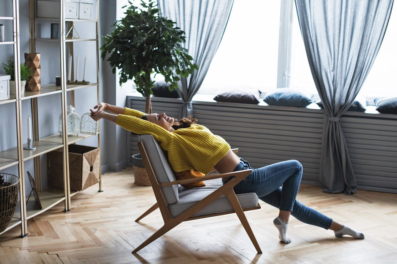 Nainen rentoutuu modernissa sirossa nojatuolissa valoisassa olohuoneessa