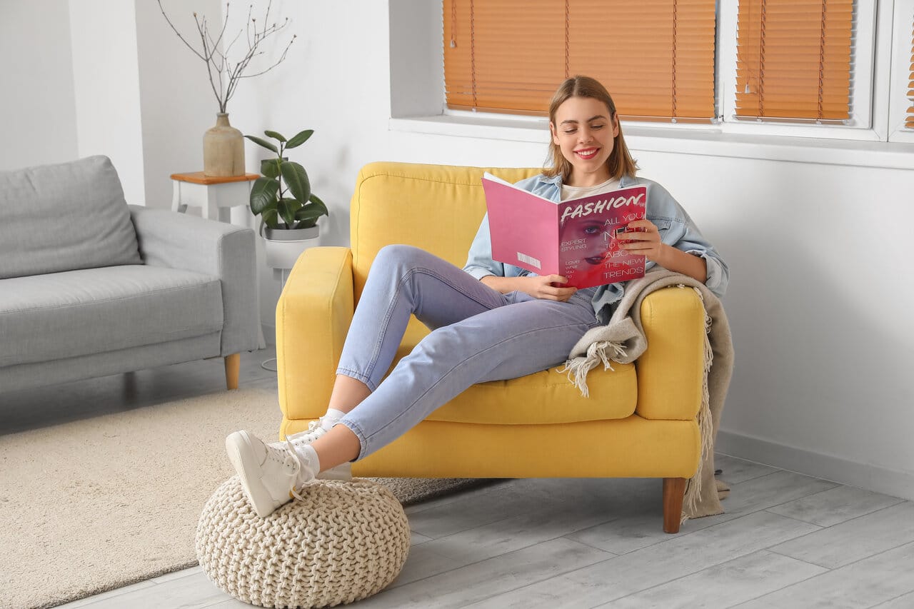 Nuori nainen istuu ja lukee lehteä modernissa keltaisessa nojatuolissa olohuoneessa.