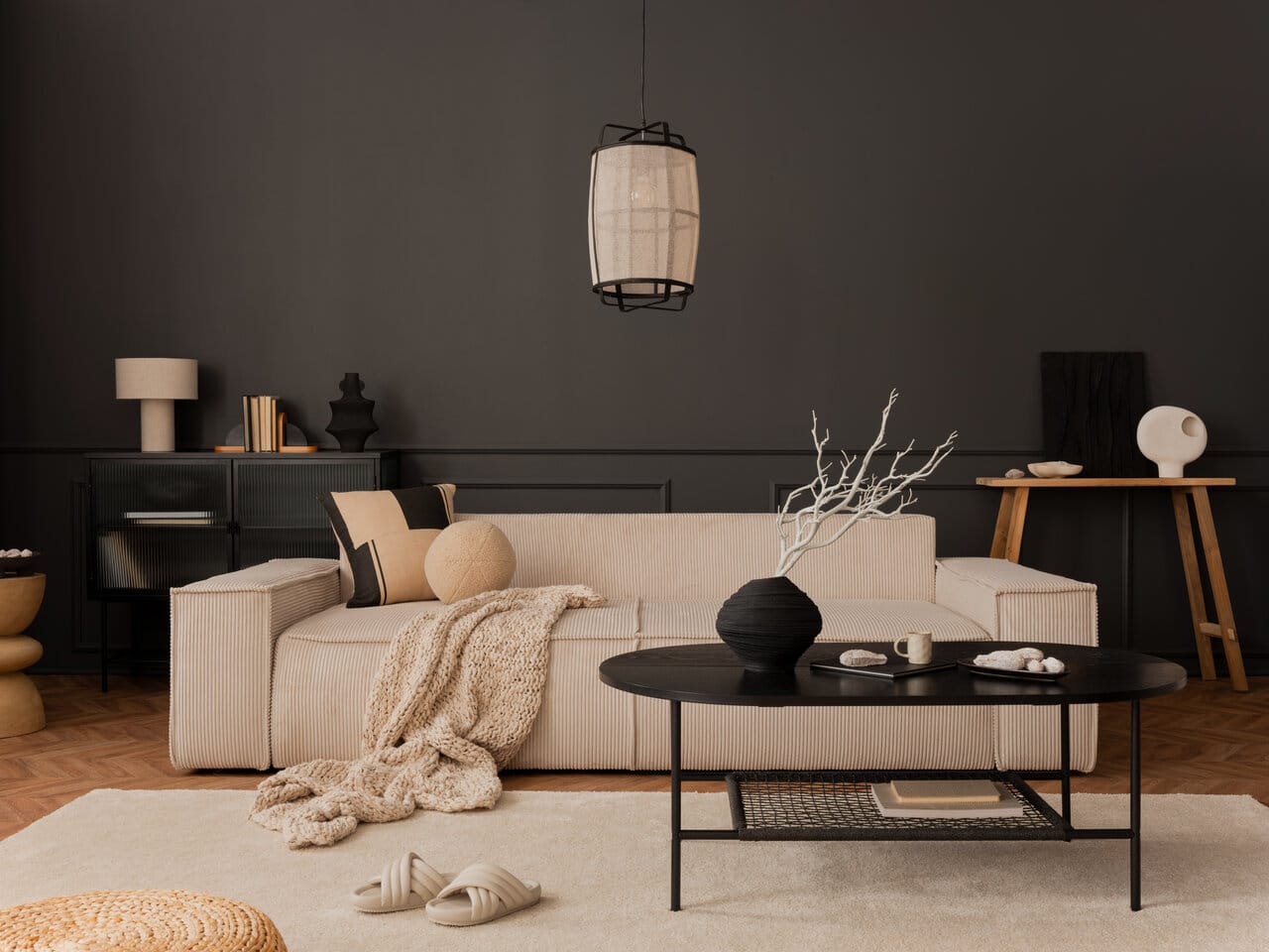 Moderni olohuone, jossa on musta ovaali sohvapöytä metallijalalla ja säilytyshyllyllä, vaalean sohvan ja tumman seinän edessä.