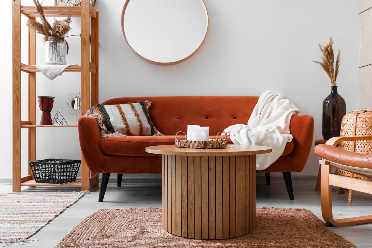 Moderni olohuone, jossa pyöreä sohvapöytä puupinnalla ja oranssi samettisohva taustalla.