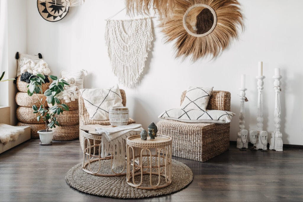 Boho-sisustettu nurkkaus, jossa punottuja huonekaluja, makramee-seinäkoriste ja luonnonmateriaaleja
