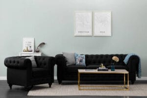 Musta Chesterfield Lyx -sohva ja nojatuoli klassisessa olohuoneessa, jossa kultakehyksinen sohvapöytä