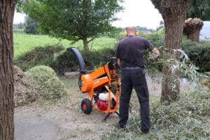 Mies syöttää oksia oranssiin polttomoottorikäyttöiseen oksasilppuriin pihapiirissä