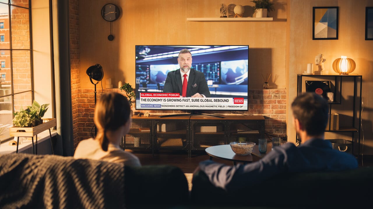 Pariskunta katsoo uutisia olohuoneessa, jossa on teollistyylinen tamminen TV-taso