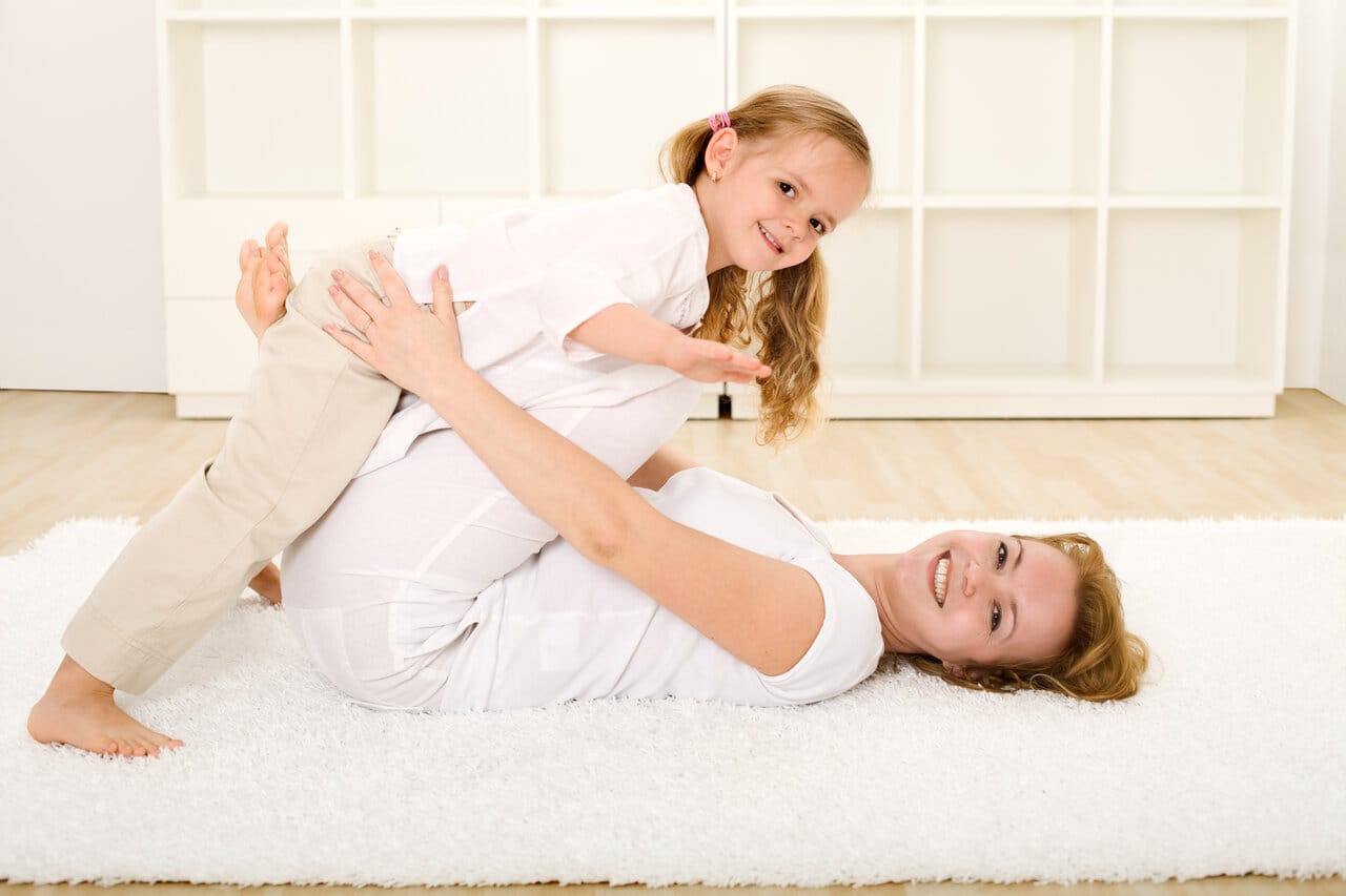 Äiti ja lapsi leikkivät valkoisella nukkamatolla valoisassa olohuoneessa