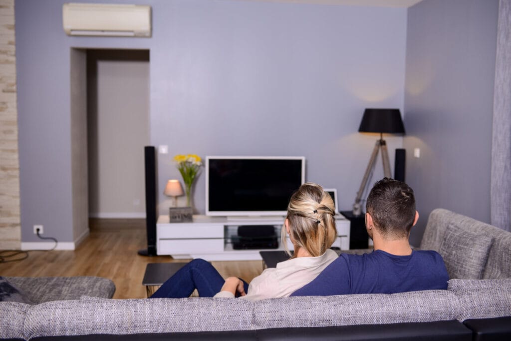 Pariskunta katsoo televisiota olohuoneessa, jossa valkoinen TV-taso ja moderni sisustus