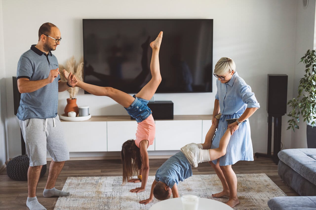 Perhe leikkii olohuoneessa ison maton päällä, taustalla TV-taso ja moderni sisustus – artikkelin kansikuva