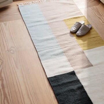 Kelim-matto 70x180 cm eteisessä, monivärinen geometrinen kuosi ja vaaleat tohvelit sen päällä