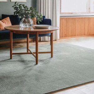 Kuva vihreästä VM Carpet Puuteri nukkamatosta olohuoneessa, jossa pyöreä puupöytä ja sininen sohva