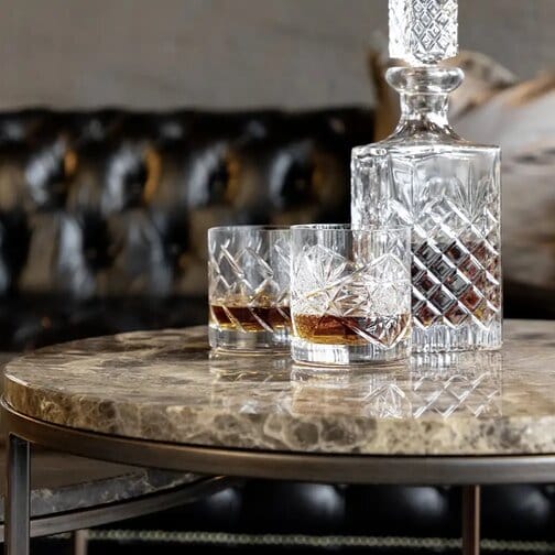 Cedes-sohvapöytä ruskeasta marmorista, päällä kristallikarahvi ja viskilasit, taustalla musta Chesterfield-sohva