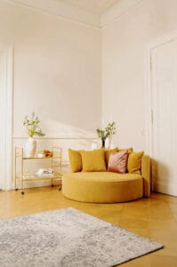 Jotexin keltainen WYOMING 2-istuttava pyöreä sohva valoisassa olohuoneessa kukkien ja juomavaunun vieressä