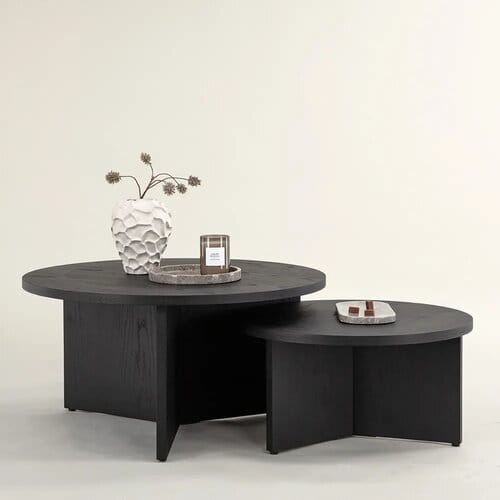 Kaksi pyöreää mustaa sohvapöytää päällekkäin vaaleaa taustaa vasten, koristeina maljakko ja tarjotin