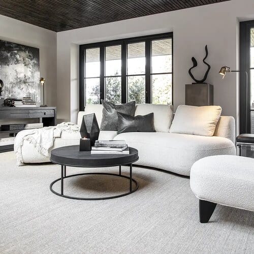 Musta pyöreä sohvapöytä modernissa olohuoneessa vaalean kulmasohvan edessä