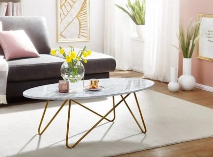 Ovaali sohvapöytä, jossa valkoinen marmorikuvio ja kultaiset metallijalat, olohuoneessa vaalean maton päällä