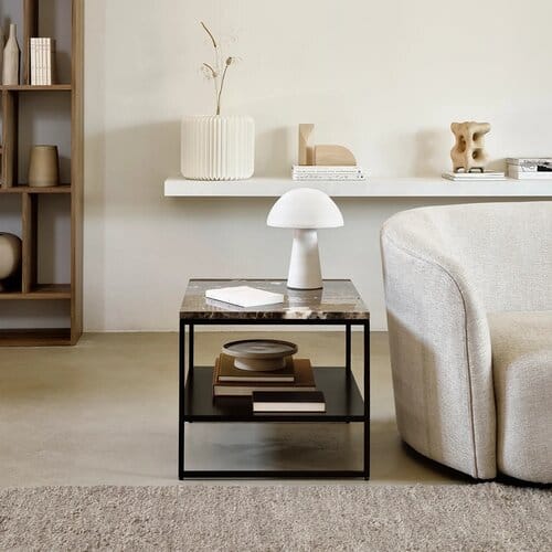 Moderni sivupöytä tummasta Emperador-marmorista ja mustasta metallista vaalean nojatuolin vieressä